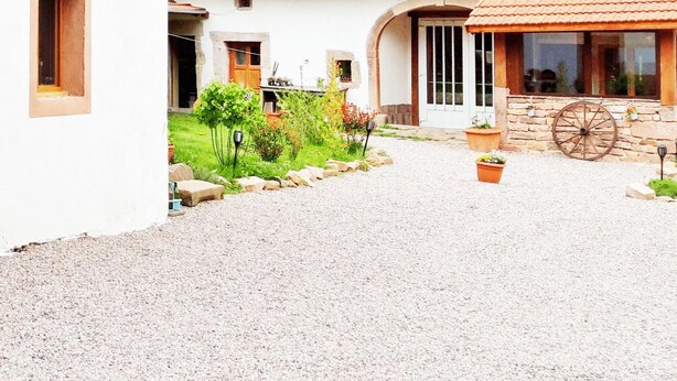 A building with a gravel driveway, a stone wall, and a wooden wheel. - renovated farmhouse for groups and families in nature, dogs welcome, playground (La Chapelle-devant-Bruyères)