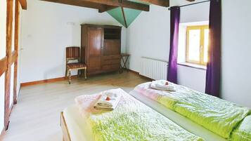 Een kamer met twee eenpersoonsbedden, houten meubels, een radiator en een raam met gordijnen.