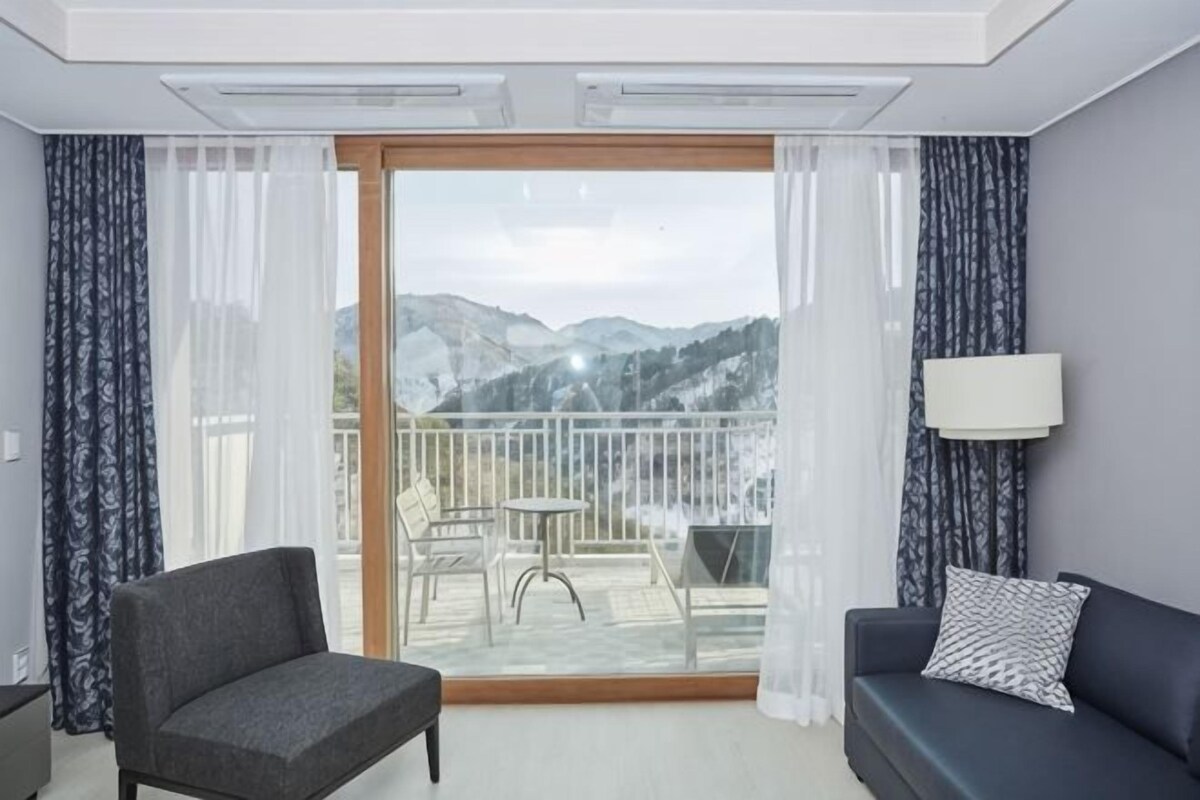 Una habitación de hotel con balcón, sofá, sillón y mesa.