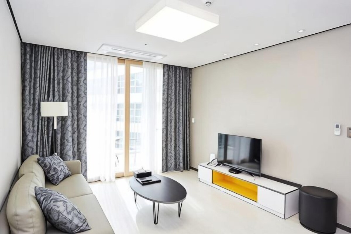 Una sala de estar moderna con sofá, mesa de centro, televisor y una ventana con cortinas.