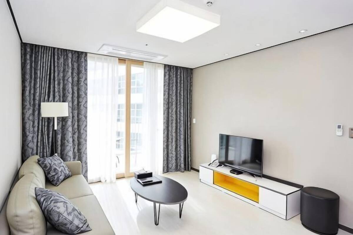 A modern living room with a sofa, coffee table, TV, and a window with curtains.
