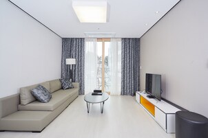Una sala de estar moderna con sofá, una mesa de centro, un televisor sobre un mueble bajo y una ventana con cortinas.