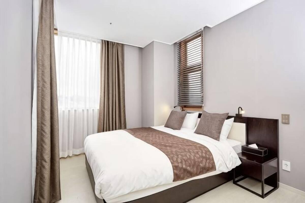 A modern hotel room with a large bed, a bedside table, and a window with blinds.