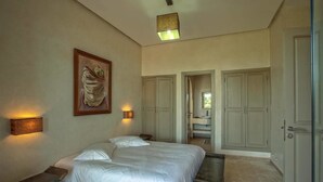 A bedroom with a large bed, a nightstand, a painting, and a bathroom visible through an open door. - Villa De Luxe Samanah (Marrakech)
