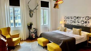 A bedroom with a bed, a yellow armchair, a small table with a vase, and a wall with a skull decoration.