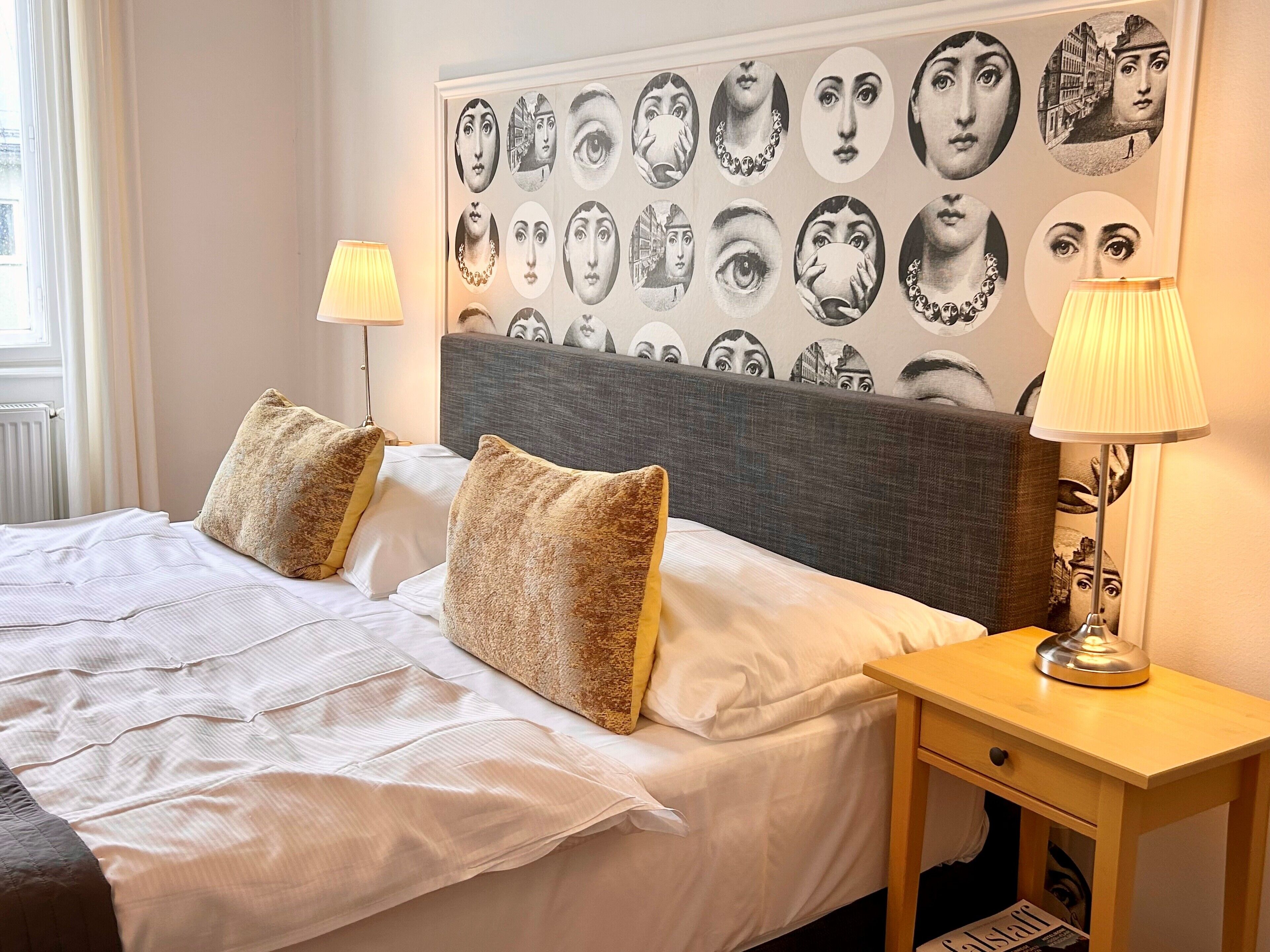 A neatly made bed with two pillows, a bedside table with a lamp, and a wall with a series of circular portraits.
