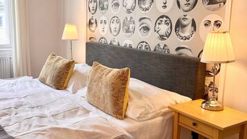 A neatly made bed with two pillows, a bedside table with a lamp, and a wall with a series of circular portraits.