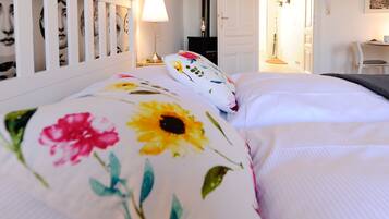 A neatly made bed with floral pillows, a bedside table with a lamp, and a wall with framed pictures.
