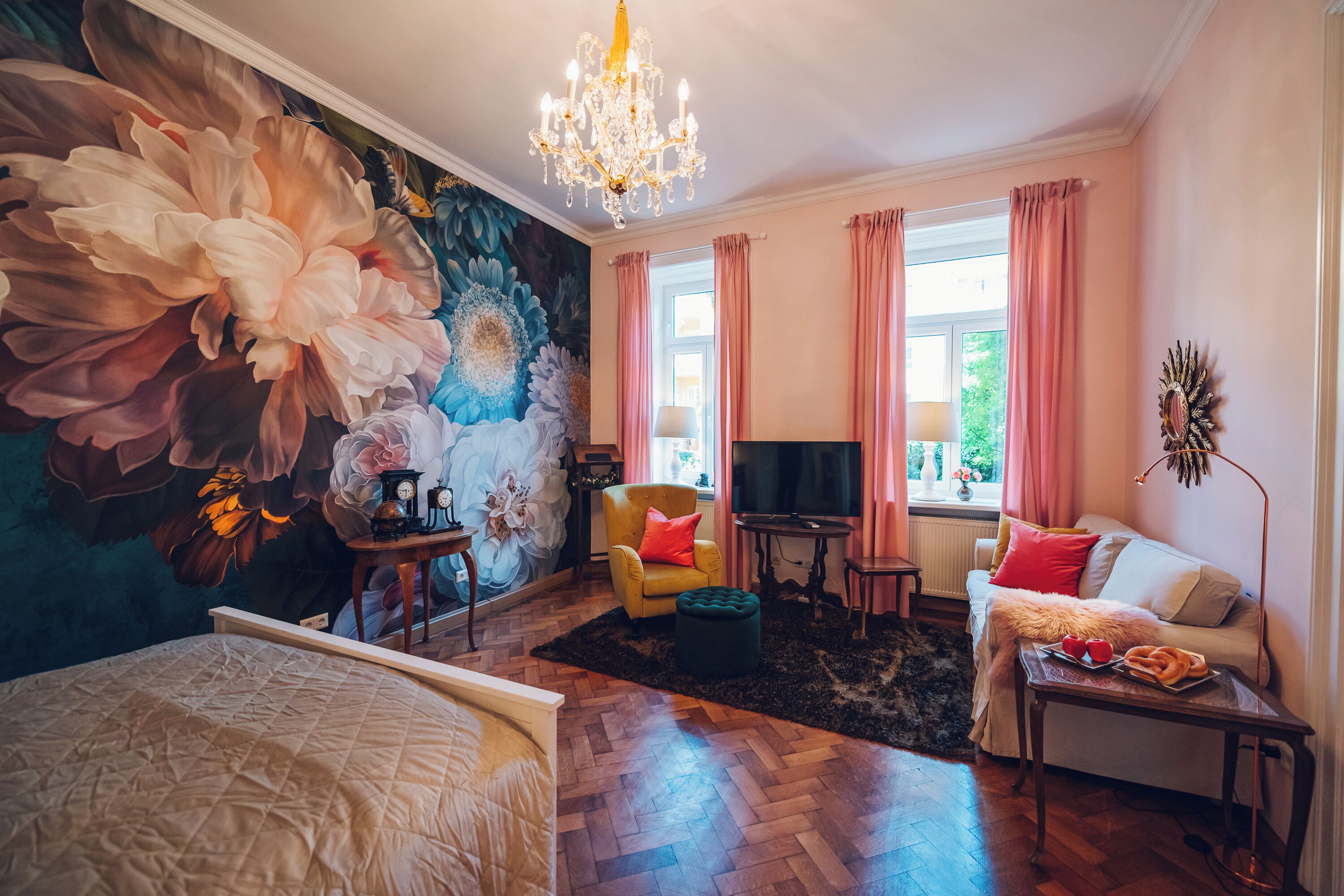 Ein Zimmer mit einer großen Blumenmalerei, einer Chandelier, einem Sofa mit Kissen, einem Fernseher und einem Holzboden.
