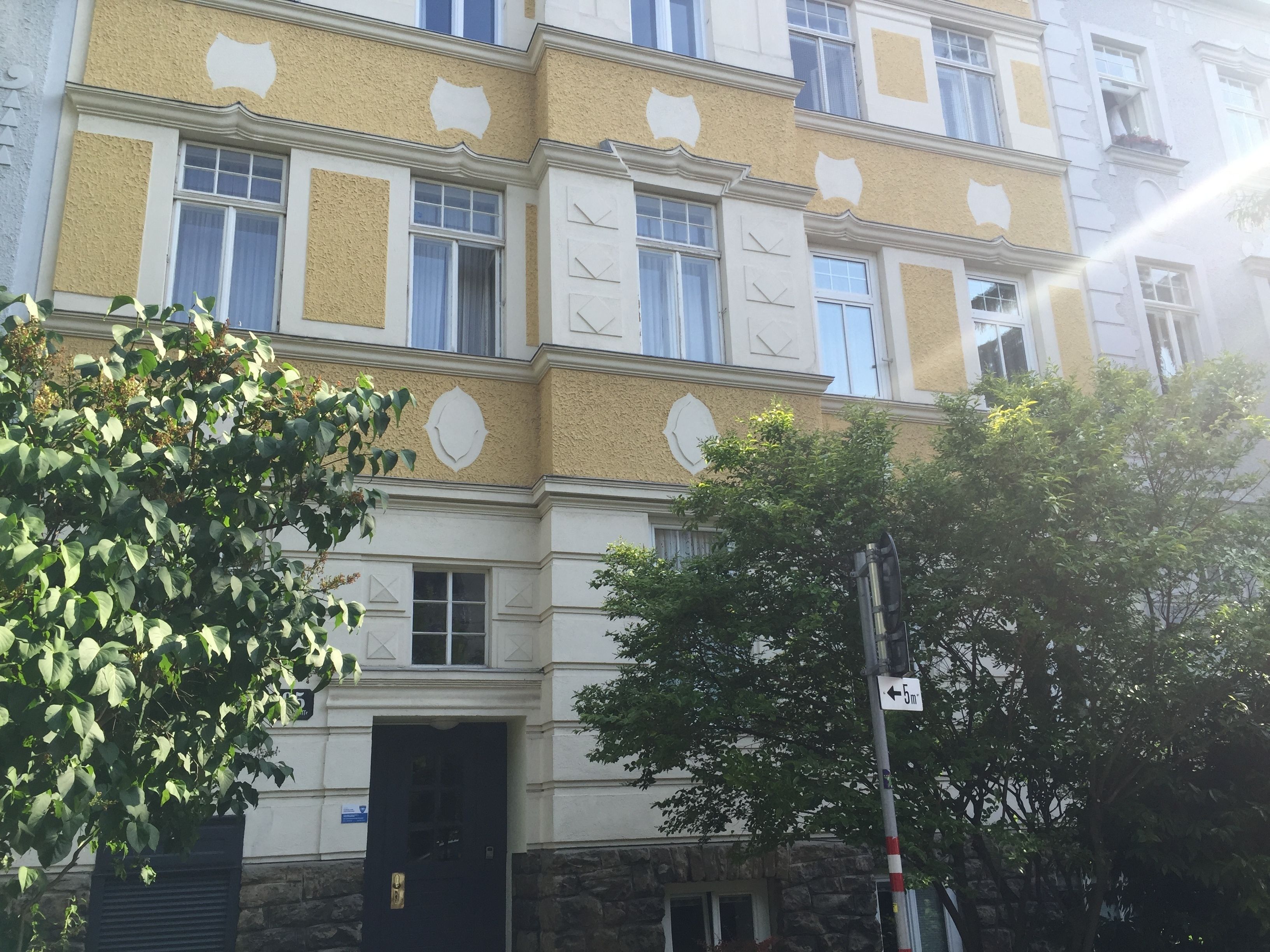 Ein mehrstöckiges Gebäude mit steinernem Sockel und gelben Wänden, mit zahlreichen Fenstern und einer schwarzen Tür.