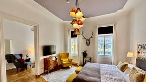 Une chambre bien éclairée, avec un lit, une télévision, une chaise, une commode et une grande fenêtre.