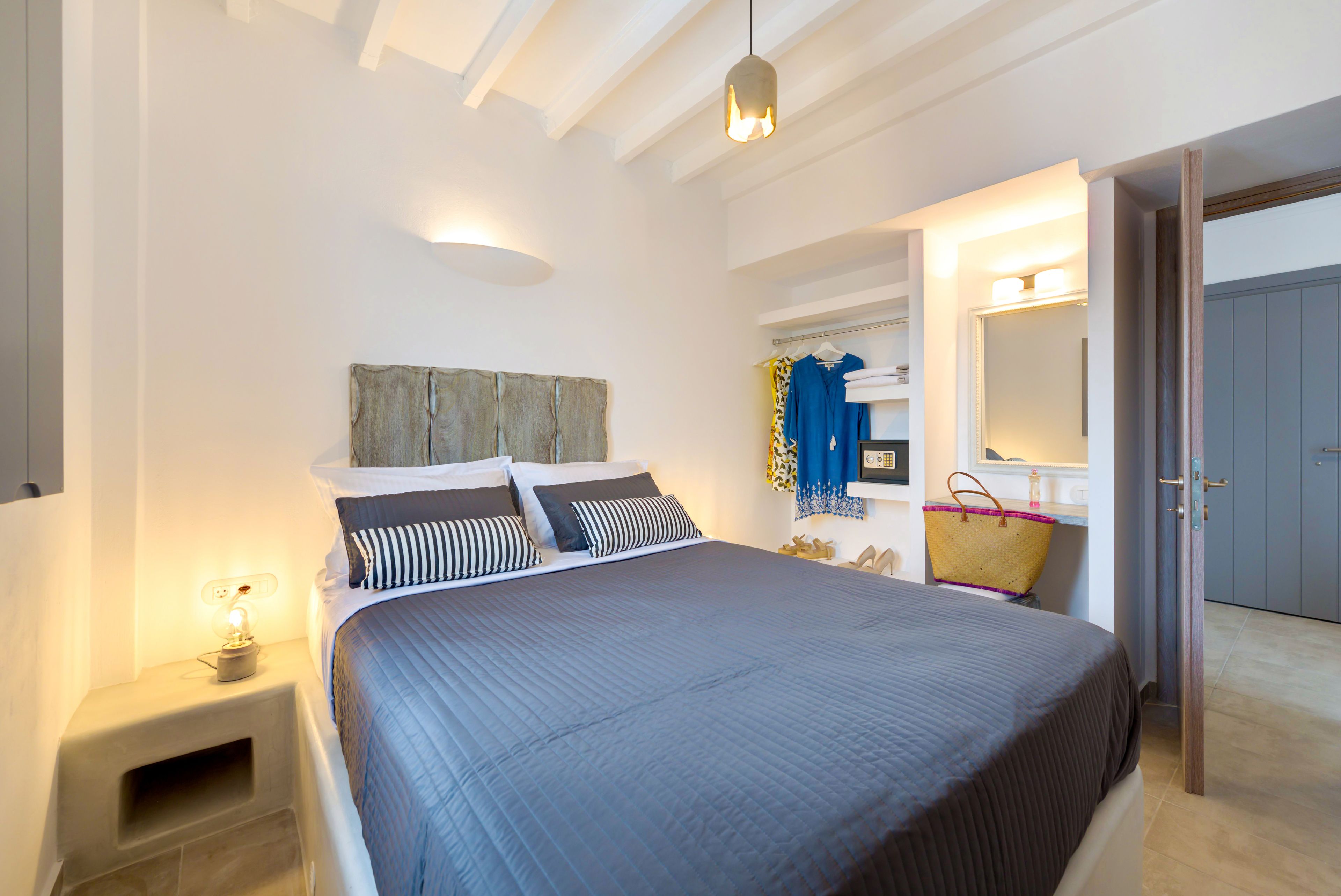 A bedroom with a large bed, bedside table with a lamp, a mirror, and a wardrobe.