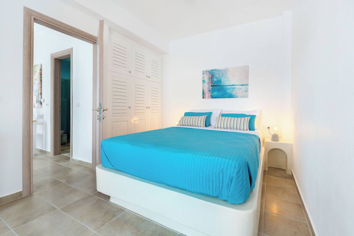 Una camera da letto con un letto, un comodino, un quadro e una porta che dà su un'altra stanza.
