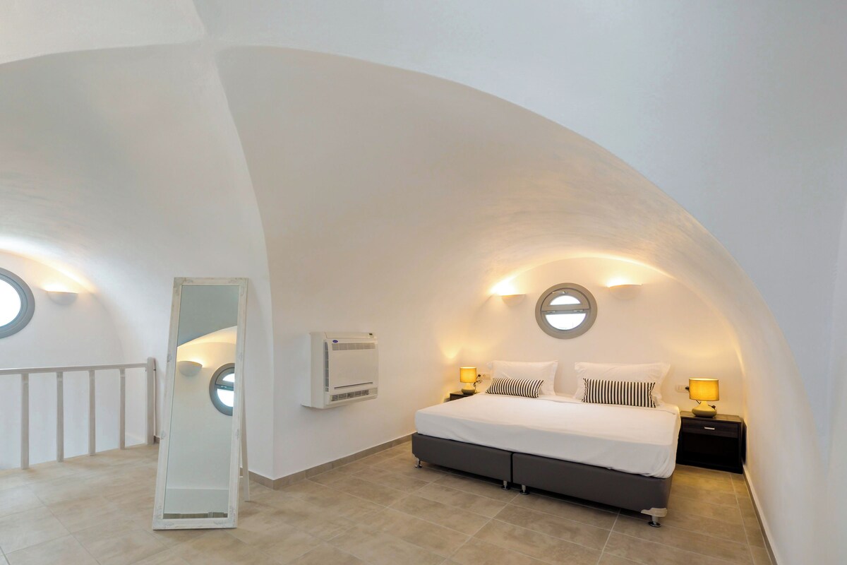 A bedroom with a curved ceiling, a bed with two pillows, a nightstand, and a wall-mounted air conditioner.