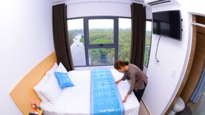 Quarto de hotel com uma cama grande, uma televisão presa na parede e uma janela com vista para o rio e vegetação.
