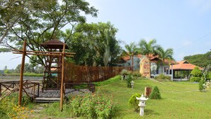 Um jardim com um parquinho de madeira, um caminho e um edifício com telhado vermelho.