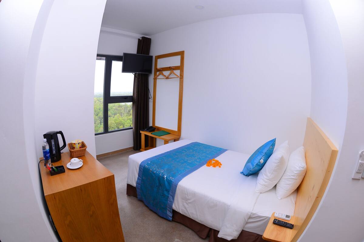 Ein Hotelzimmer mit einem Bett, einem Schreibtisch mit Wasserkocher, einem Fernseher und einem Fenster mit Blick.