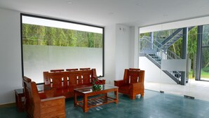 Um quarto espaçoso com uma janela ampla, um conjunto de sofás de madeira, uma mesa de centro e uma escada visível através da janela.