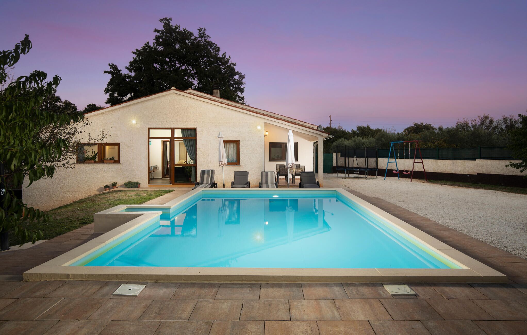 Ein Haus mit Swimmingpool, Terrasse mit Stühlen und einer Schaukel.