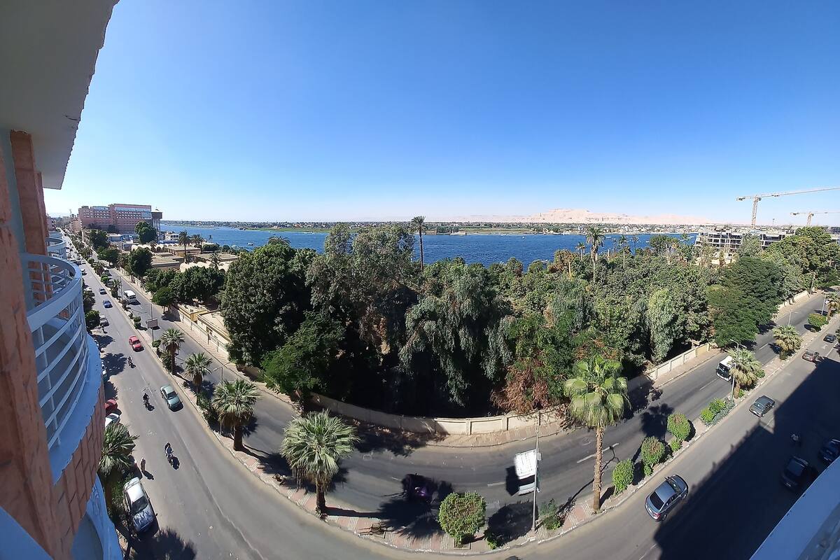 A high vantage point view of a coastal city with a clear blue sky, a road with vehicles, and a body of water in the distance.