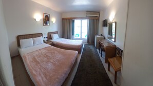 Habitación de hotel con dos camas, un escritorio, una silla, un televisor y una ventana con cortinas.