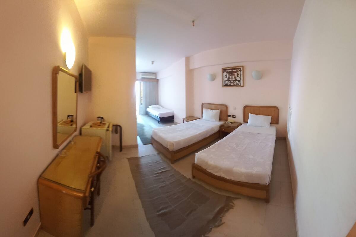 A hotel room with two single beds, a wooden dresser, a desk, and a mirror.