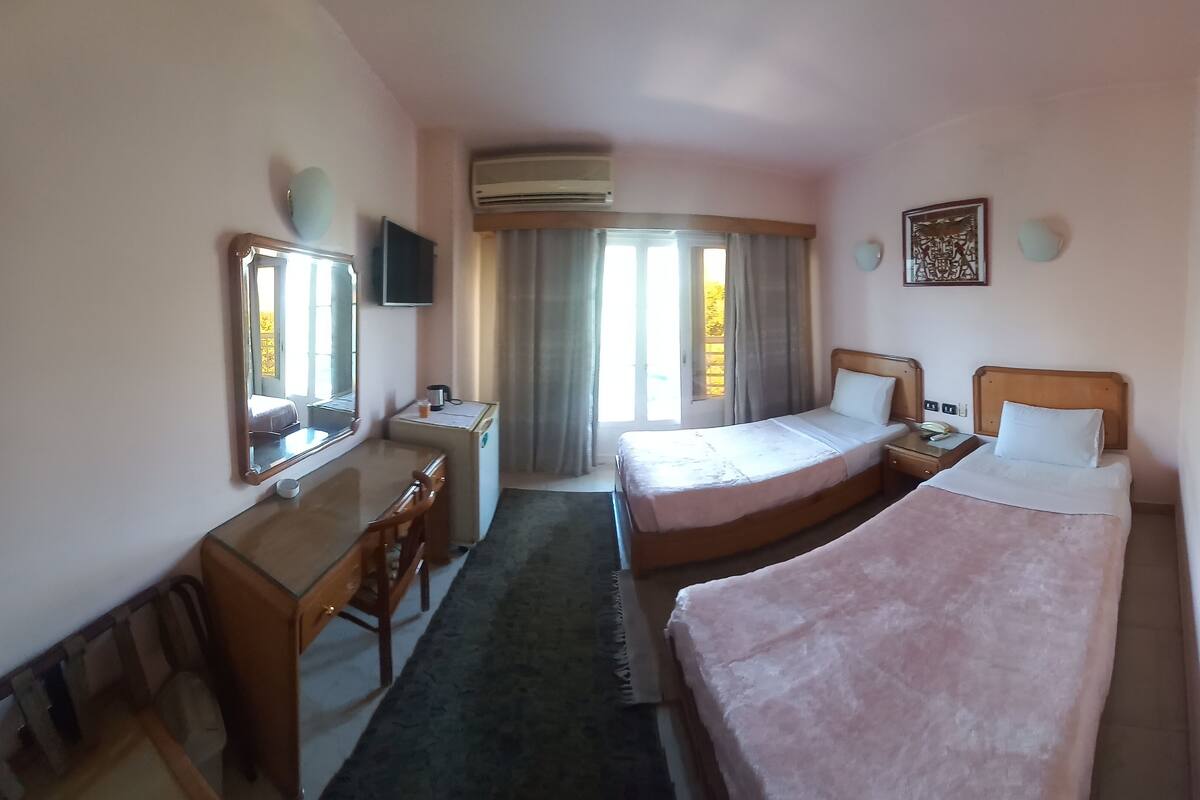 A hotel room with two single beds, a desk with a chair, a small table, and a mirror.
