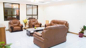 A spacious living room with leather sofas and armchairs, a coffee table, and a large window providing natural light.