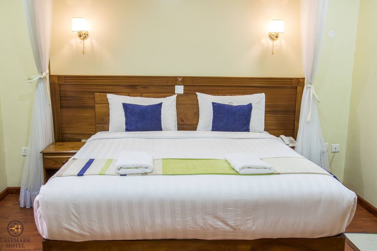 Habitación de hotel con cabecera de madera, dos lámparas de noche, una cama con ropa blanca y un teléfono en la mesita de noche.
