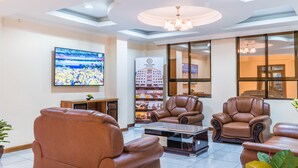 A hotel lobby with leather sofas, a large flat-screen TV, a reception desk, and a chandelier. - Eastmark Hotel (Nakuru)