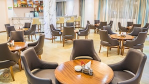 A hotel lobby with round tables and chairs, a bar area, and a marble column. - Eastmark Hotel (Nakuru)