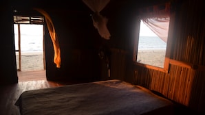 A room with a bed, wooden walls, and a view of the beach. - Reva Castel (Nosy Be)