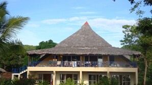 A building with a thatched roof, a balcony with blue railings, and a pool area. - Reva Castel (Nosy Be)