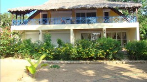 A two-story building with a thatched roof and a balcony with blue railings. - Reva Castel (Nosy Be)