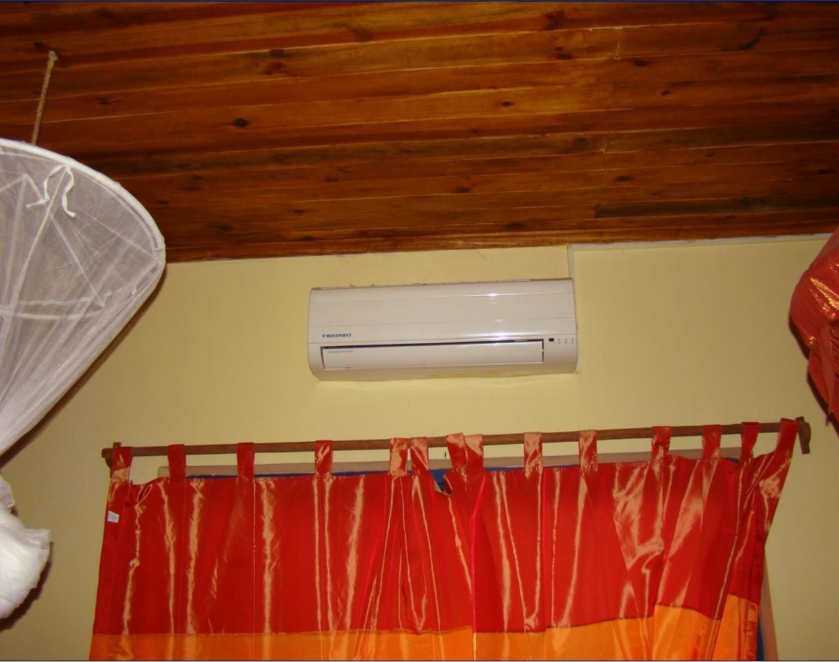 A room with a wooden ceiling, an air conditioning unit, and a red and orange striped curtain.