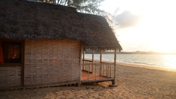 A beach hut with a thatched roof, wooden deck, and a view of the sea. - Reva Castel (Nosy Be)