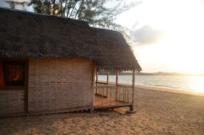 A beach hut with a thatched roof, wooden deck, and a view of the sea. - Reva Castel (Nosy Be)