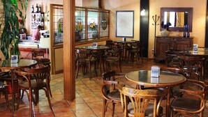 Ein Restaurant mit runden Tischen, Holzstühlen, einer Bar und einer großen Pflanze.