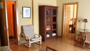 Ein Zimmer mit Holzboden, Schaukelstuhl, Glastisch, Korbstuhl und einer Holzkabine mit Glastüren.