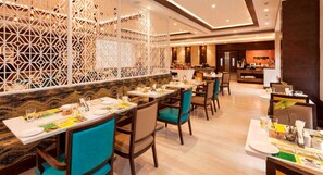 A restaurant with multiple tables and chairs, a decorative partition, and a counter area in the background. - Lemon Tree Hotel Lucknow (Lucknow)
