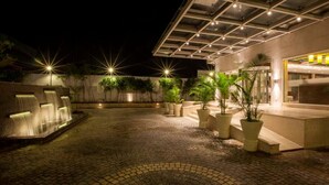 Un patio con una fuente de agua, plantas en macetas y un edificio con fachada de vidrio.