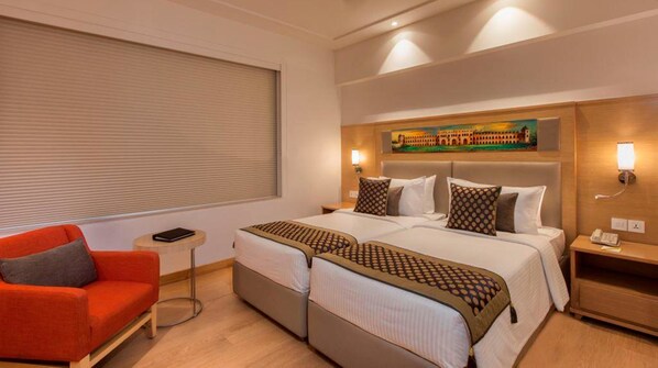 A hotel room with two beds, a red sofa, a small table, and a painting on the wall.