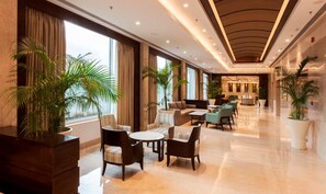 Un vestíbulo amplio con techo alto, ventanas grandes y una variedad de zonas de estar, incluyendo sofás y sillones.