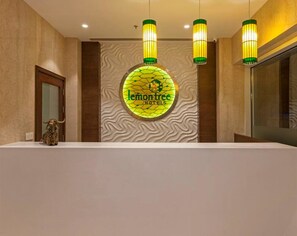 A reception area with a circular logo for 'lemon tree hotels' on the wall, three hanging pendant lights, and a reception desk. - Lemon Tree Hotel Lucknow (Lucknow)
