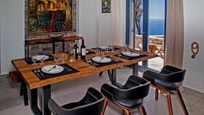 A dining area with a wooden table set for six, black chairs, and a view of the sea through a glass door. - Villa Asterope, Luxury Retreat by Pleiades (Santorini)
