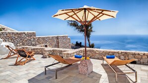 A terrace with two wooden lounge chairs, a stone wall, and a view of the sea. - Villa Asterope, Luxury Retreat by Pleiades (Santorini)