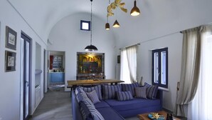 A modern living room with a blue sofa, a wooden coffee table, and a kitchen in the background. - Villa Asterope, Luxury Retreat by Pleiades (Santorini)