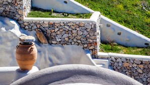 A stone wall with a rustic terracotta pot and a stone bench. - Villa Asterope, Luxury Retreat by Pleiades (Santorini)