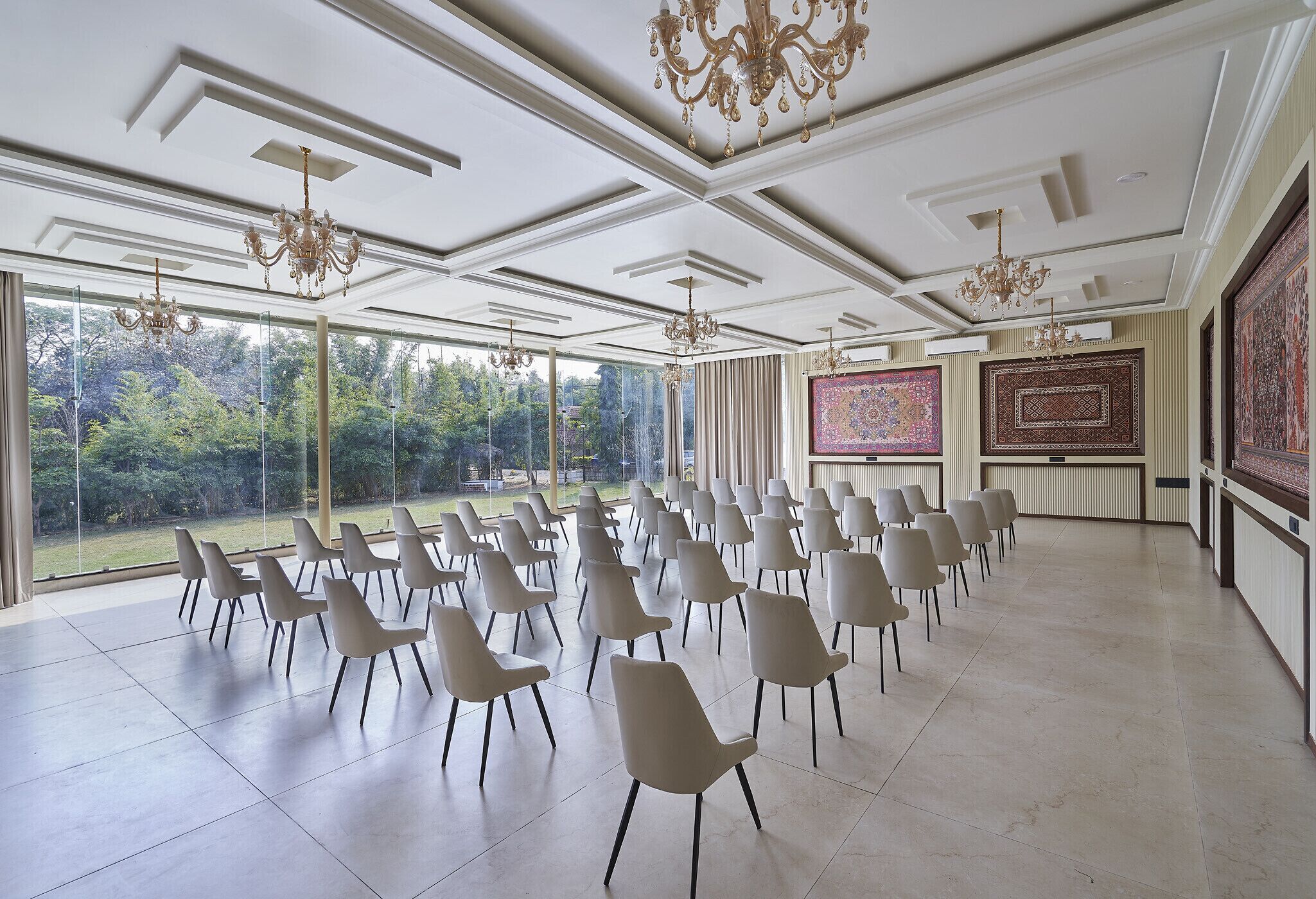 A spacious room with rows of chairs, large windows, and chandeliers.
