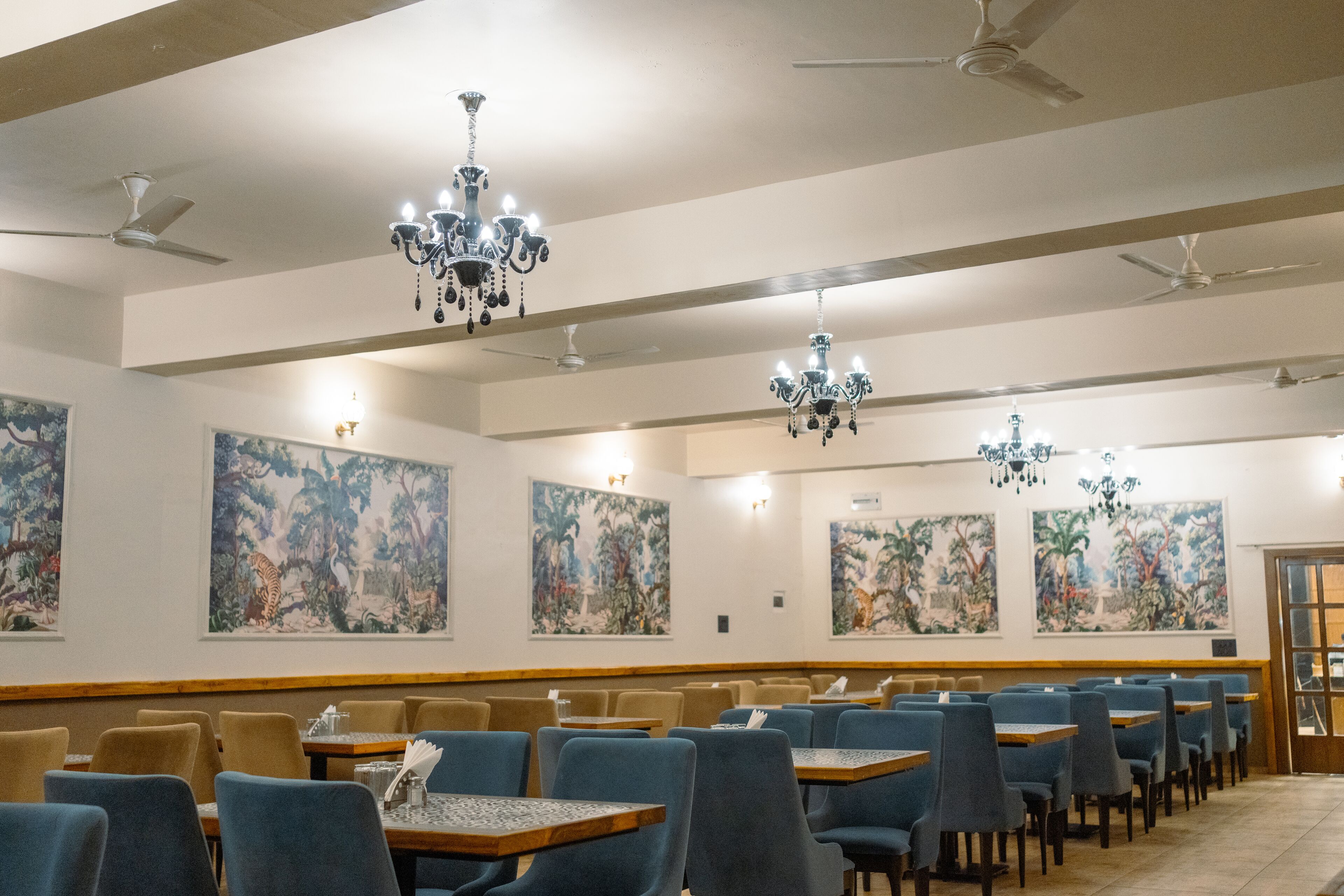 A restaurant with blue chairs, wooden tables, and chandeliers.